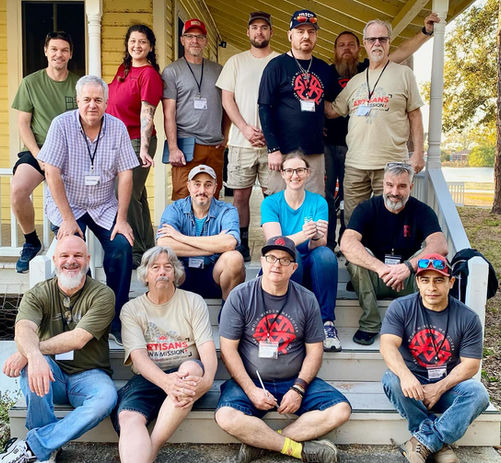 Workshop graduates seated together on the steps of a historic house